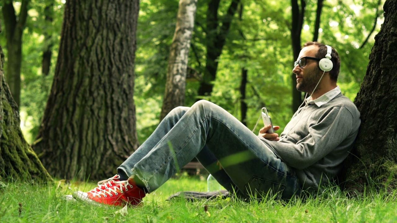 Is the man listening. Read book in Park. Listen to Music in the Park. Man sitting in nature. Lonely person in the Park.