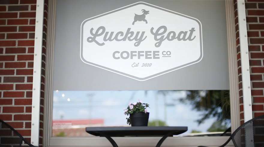 Lucky Goat Coffee store from the outside with a table and a flower on it.